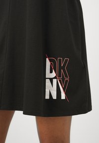 Czarna bawełniana koszulka z odważnym nadrukiem "DKNY" w białym i czerwonym kolorze, z ukośną czerwoną linią przecinającą litery.