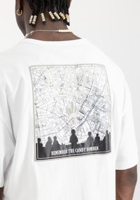 Camiseta blanca con un gráfico de mapa en blanco y negro con siluetas en la parte inferior y el texto "RECUERDA AL BOMBERO DE DULCES".