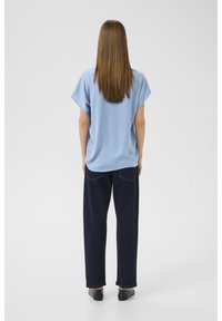 Top azzurro chiaro a maniche corte con una vestibilità comoda, abbinato a jeans a gamba larga blu scuro. Texture liscia e design semplice, visto da dietro.