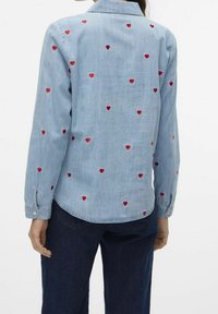 Camicia in denim azzurro chiaro con ricami a forma di cuore rossi sparsi, maniche lunghe, polsini con bottone e colletto.