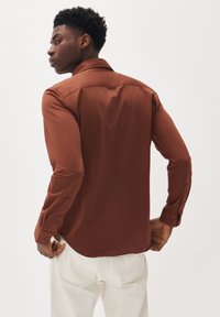 Bruine longsleeve shirt gemaakt van een gladde, glanzende stof. Beschikt over een klassieke kraag, knoopmanchetten en een licht gebogen zoom.