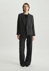 Costume à rayures noires et grises comprenant un blazer croisé et un pantalon à jambes larges, fabriqué à partir d'un tissu texturé.