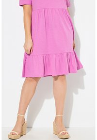Vestido rosa de manga corta con dobladillo en capas, hecho de una tela suave. Lleva sandalias de cuña beige con tiras para el tobillo.