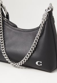 Schwarze Leder-Schultertasche mit geschwungenem Profil, silberner Kettenhenkel und kleinem Markenlogo an der Seite. Reißverschlussverschluss oben.
