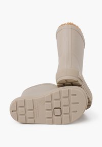 Botas de goma beige con una superficie texturizada, punta redonda y un borde superior acolchado y suave. Suelas planas y con patrón para mayor tracción.