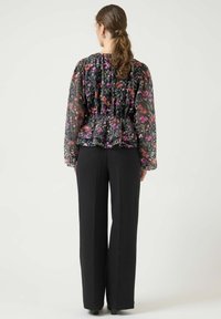 Blomstret peplumbluse i gjennomsiktig svart stoff, med fargerike blomster. Kombinert med høytlivede svarte bukser, som skaper en avslappet silhuett.