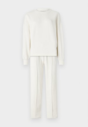 Baltas, garajam piedurkņu džemperis ar noapaļotu kakla izgriezumu un ribotām aprocēm, komplektā ar saskaņotām taisnām biksēm ar vertikālām šuvēm.