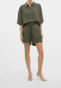 Camicia verde oliva a maniche corte con bottoni abbinata a pantaloni corti con cordoncino. Tessuto morbido con vestibilità rilassata. Sandali con tacco color crema.