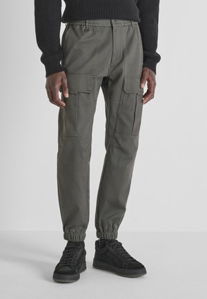Pantalones cargo en verde oliva oscuro con cintura elástica, piernas entalladas, múltiples bolsillos y tela texturizada. Combinados con zapatillas negras.
