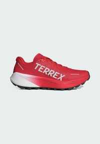 Chaussure de trail running rouge avec talon à dégradé blanc et semelle épaisse noire, marquée "TERREX" sur le côté, conçue pour les activités de plein air.