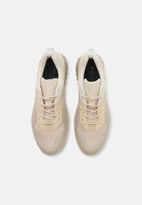 Beige treningssko med teksturert mesh-overdel, polstret krage og lette lisser. De har en fleksibel gummisåle med mønstret grep.