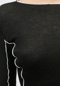 Czarny prążkowany sweter z białym falistym obszyciem przy dekolcie i szwie ramienia, charakteryzujący się miękką, lekko prześwitującą teksturą.