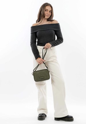 Olive green crossbody bag with a textured surface and decorative stitching. Model wears a black off-shoulder top and wide white pants.
