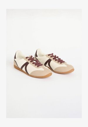 Beige un krēma krāsas sporta apavi ar brūniem akcentiem, ar gludu augšdaļu, gumijas zoli un vieglām auklām. Retro dizains ar izsmalcinātu formu.