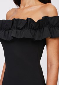 Black off-the-shoulder dress featuring a ruffled neckline. Smooth, fitted fabric with subtle sheen and seamless design.