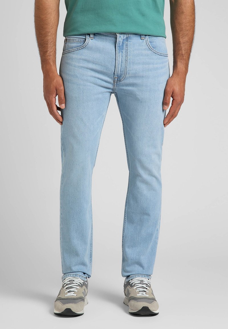 Ljust blå denimjeans med rak benstil, utrustade med fem fickor och subtila sömdetaljer, i kombination med grå och vita sneakers.