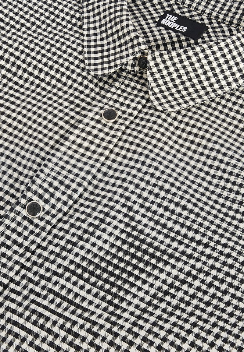 Schwarz-weiß kariertes Hemd mit Kragen und Knopfverschluss. Mit strukturiertem Stoff und einem Etikett, das "THE KOOPLES" trägt.