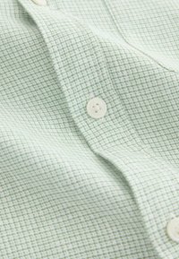 Chemise boutonnée vert clair avec un motif quadrillé texturé. Comprend des boutons blancs et une texture de tissu tissé lisse.