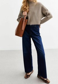 Pull tricot gris clair avec un motif texturé, pantalon large en denim foncé taille haute, et un sac fourre-tout en cuir marron avec un accent clair. Ballerines imprimé léopard.