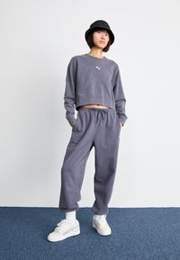 Sudadera gris recortada con puños acanalados y un pequeño logo blanco, combinada con pantalones de chándal holgados a juego y zapatillas blancas con detalles.