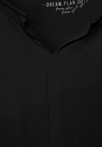 Schwarzes T-Shirt mit V-Ausschnitt, aus glattem Stoff hergestellt. Verfügt über eine zentrale Naht und einen dezent bedruckten Text im inneren Kragen.