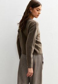Suéter marrón de punto con dobladillo acanalado, combinado con pantalones de cuadros de pierna ancha. El conjunto presenta un ajuste casual y una textura suave, visto de lado.