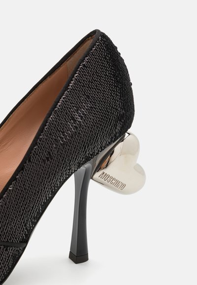 Chaussure à talons hauts noire avec un matériau texturé, bout pointu et un accent de talon en forme de cœur argenté. Présente des détails polies.