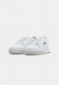 Tênis brancos de cano baixo, com atacadores, detalhes perfurados e o logo do crocodilo da Lacoste na lateral, exibidos sobre um fundo branco.