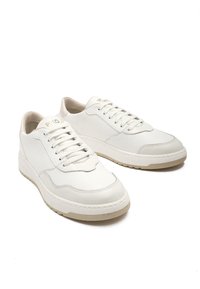 Białe skórzane trampki z fakturowanym wykończeniem, z grubą podeszwą, okrągłym noskiem i tradycyjnym zapięciem na sznurówki. Minimalistyczny akcent w designie.