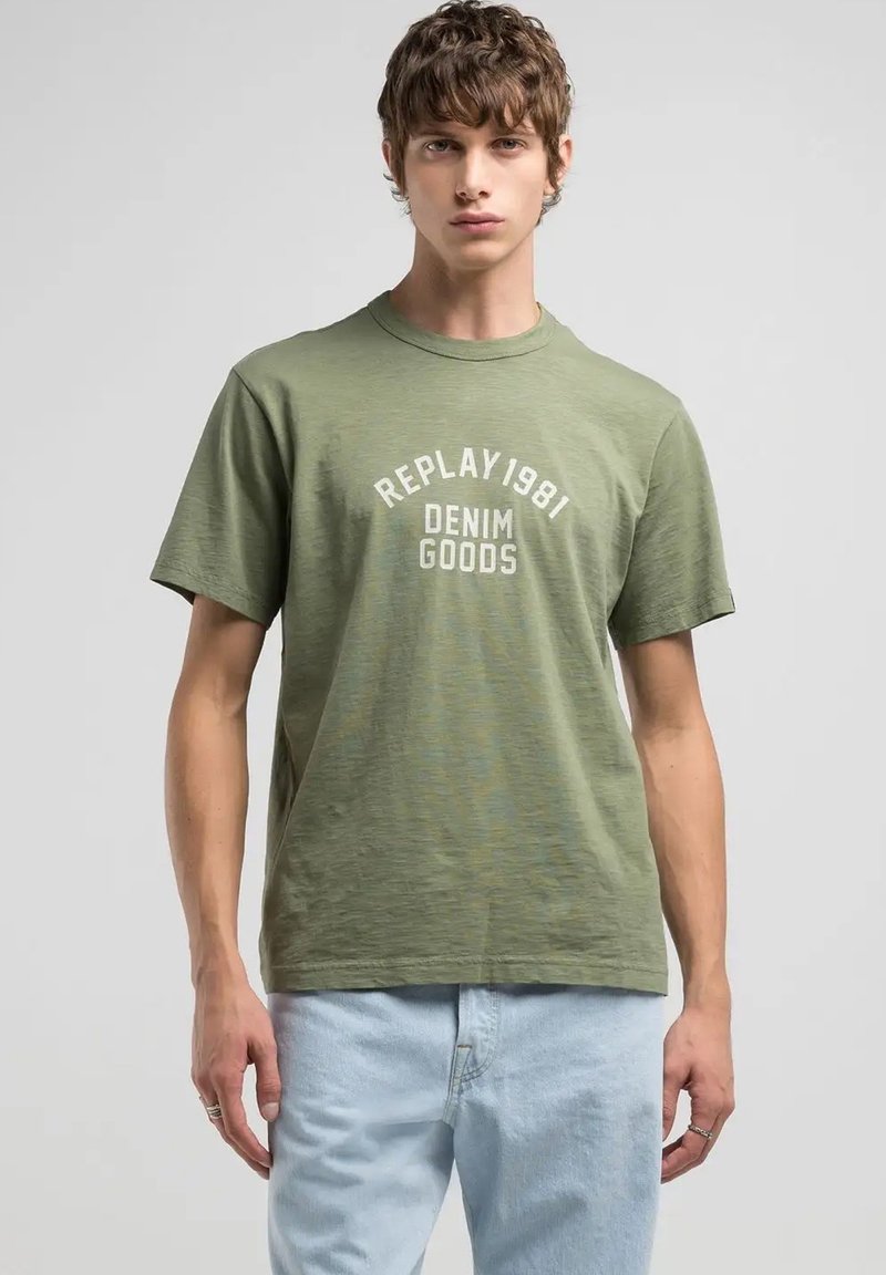 Camiseta verde oliva con cuello redondo, con texto impreso en blanco "REPLAY 1981 DENIM GOODS" en el pecho. Tejido suave y texturizado.