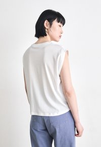 White sleeveless top with a relaxed fit, soft cotton material, and round neckline; worn with light blue, high-waisted jeans.