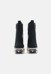 Černé plátěné kotníkové boty se zipem, gumovou podrážkou a nášivkou s logem Chuck Taylor na patě. Mají strukturovaný svršek a kontrastní podrážku.