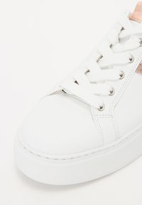 White sneaker with synthetic upper, flat laces, silver eyelets, and a metallic rose gold accent on the side. Rounded toe, thick sole.