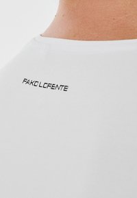 Biała bawełniana koszulka z minimalistycznym czarnym logo "PAKO LORENTE" w pobliżu dekoltu. Prosty okrągły dekolt i gładka tekstura.