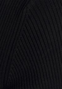 Tissu en maille noire avec une texture à côtes verticales, agrémenté de coutures diagonales formant des formes géométriques. Matériau doux et flexible.