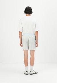 Pantalones cortos de rayas azul claro con cintura elástica, de longitud corta y detalle en el bolsillo trasero, combinados con una camiseta blanca y zapatos casuales.