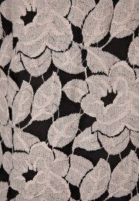 Svart tyg med stort, beige blommönster i spets, som visar detaljerade mönster av blad och kronblad på en fin nätbakgrund.