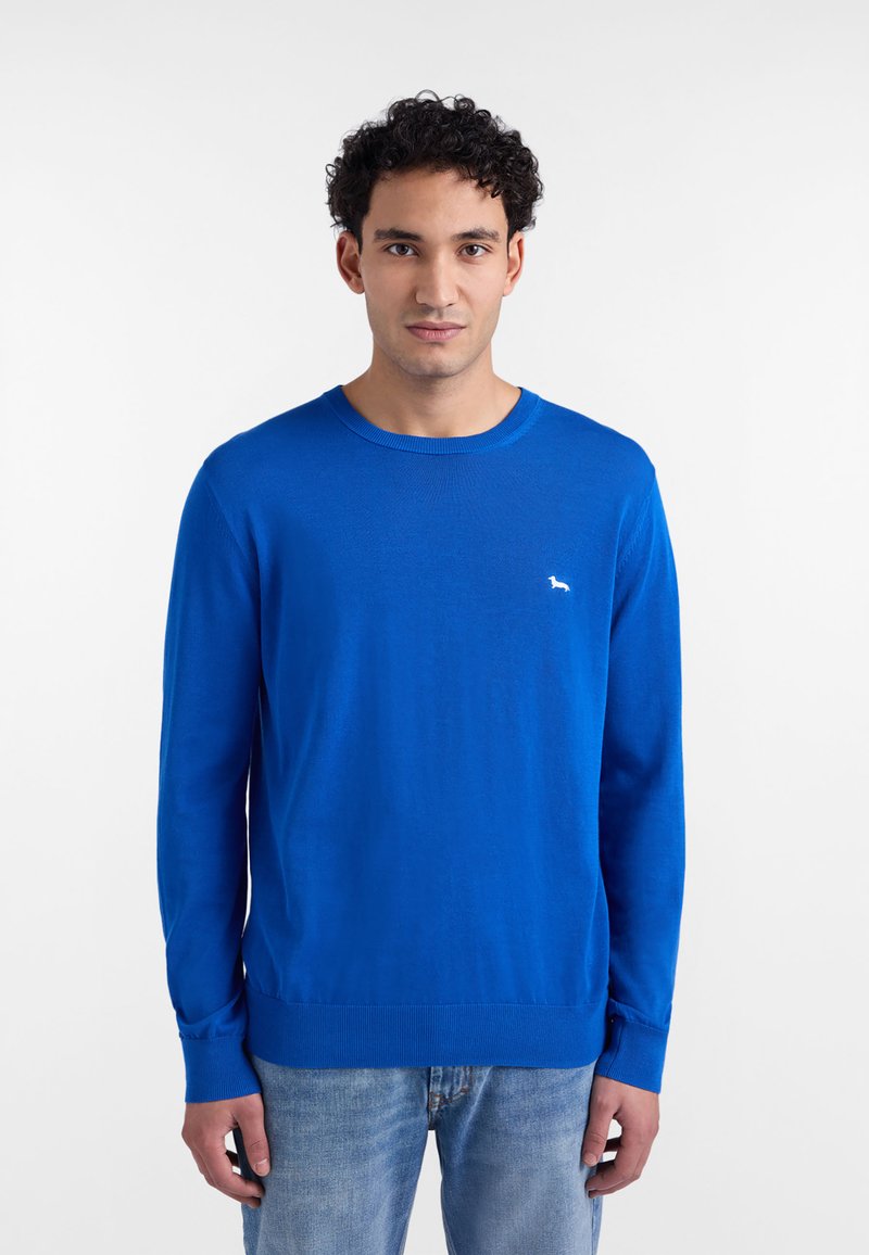 Modrý sveter s dlhými rukávmi vyrobený z ľahkej pleteniny. Má okrúhly výstrih a malú bielu značku na ľavej strane na hrudi.