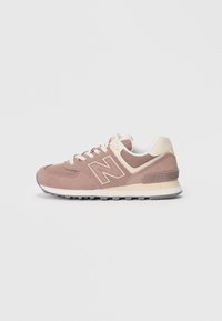 Light pink suede sneakers with cream accents, featuring a textured fabric upper, flat laces, and a rubber sole with tread pattern.