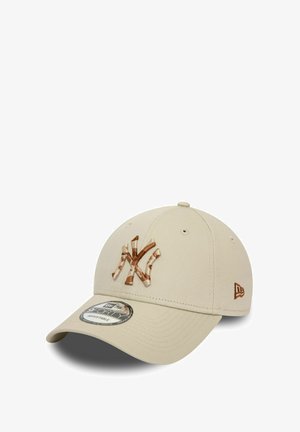 Beige baseball cap with a curved visor, featuring a brown embroidered "NY" logo and small brown accent on the side, made from fabric material.