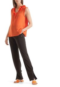 Top sin mangas naranja con escote fruncido, combinado con pantalones negros con aberturas laterales, y sandalias naranjas de tacón plano.
