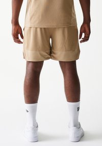 Μπεζ αθλητικό σορτς με σχέδιο από δίχτυ, με λεία μέση και πλαϊνές τσέπες, συνδυασμένο με λευκές κάλτσες και αθλητικά παπούτσια.