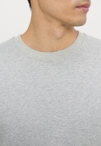 Light gray crewneck sweatshirt made of soft fabric, featuring a ribbed collar and subtle texture. No prominent patterns or accents visible.