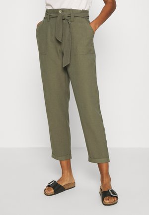 Olijfgroene op maat gemaakte broek met een riem, twee voorkruisjes en opgerolde manchetten. Draagt een paar zwarte slidesandalen met een brede band en gesp.