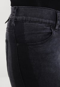 Vaqueros de denim negro desgastados con corte slim, que cuentan con una cintura alta, bolsillos frontales y detalles de costura en el mismo tono.