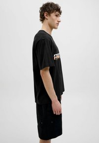 Zwarte katoenen t-shirt met korte mouwen, voorzien van een geprinte logo in een contrasterende kleur, gecombineerd met zwarte shorts tot de knie.