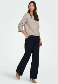 Beiger Strickpullover mit Perlenverzierungen, kombiniert mit hoch taillierten, marineblauen Jeans mit weitem Bein und nudefarbenen, spitz zulaufenden High Heels.