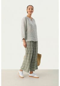 Lichtgrijze linnen overhemd met lange mouwen, gecombineerd met groene broek met brede pijpen en witte sneakers. Inclusief een geweven tas als accessoire.