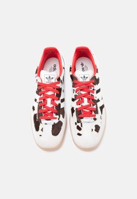 Λευκό αθλητικό παπούτσι με μαύρο μοτίβο δέρματος αγελάδας, κόκκινα κορδόνια και λευκό σχέδιο τριών ρίγων. Σόλες από καουτσούκ και επένδυση εσωτερικά σε κόκκινο χρώμα. Ρυθμιζόμενο κλείσιμο με κορδόνια.