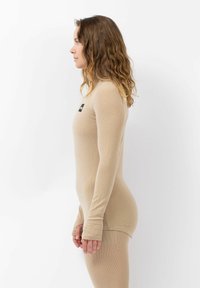 Haut beige à manches longues en tissu côtelé, présentant un design ajusté et des ouvertures pour les pouces au niveau des poignets, présenté sur un fond blanc.